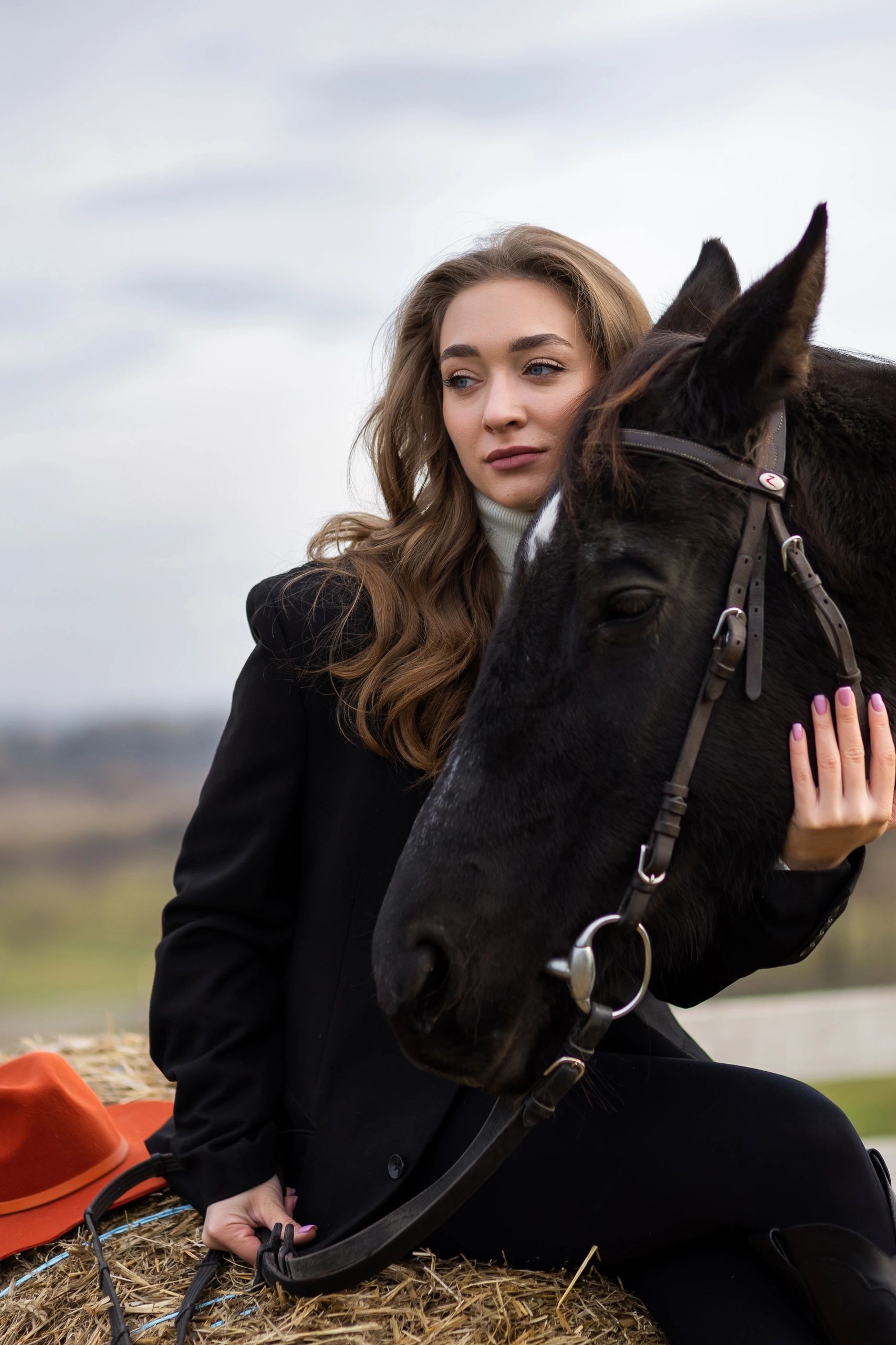 Woman seated beside black horse outdoors